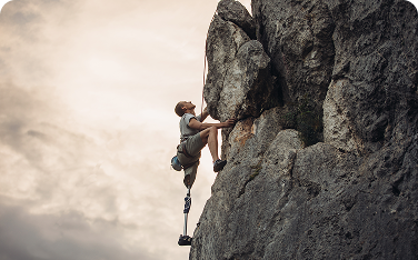 A person with a prosthetic leg climbing a steep rock face, gripping the stone with determination. The cloudy sky behind them highlights the strength and courage of their ascent.